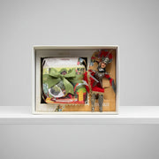 Gift set with a nutcracker figure, wrapped items, and a spoon in a box on a gray background