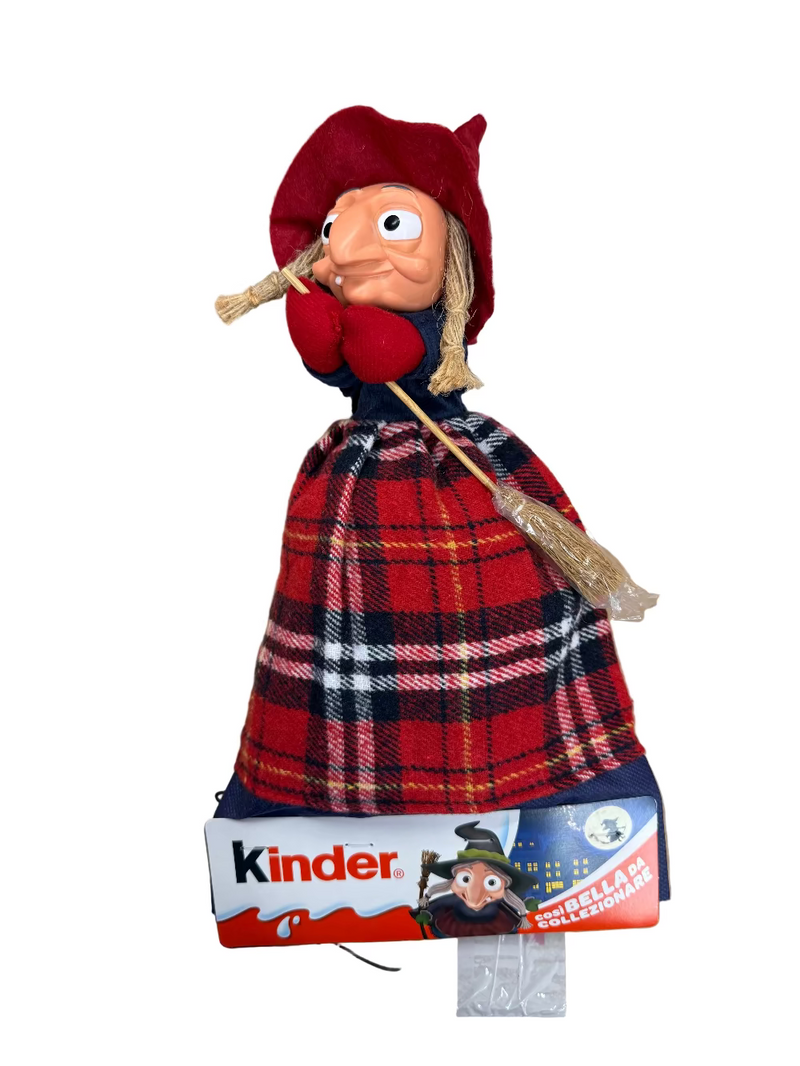 Toy figure of a character in a red hat and plaid dress with a broom, on a Kinder packaging background.
