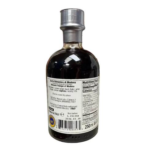 Bottle of Aceto Balsamico di Modena on a kitchen counter with various items in the background.