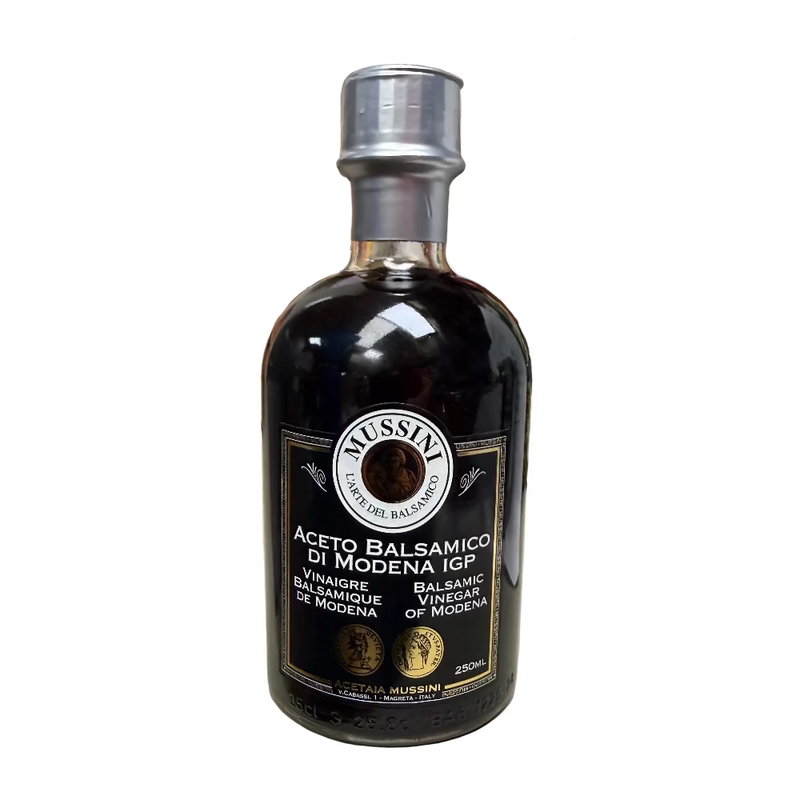 Bottle of Mussini Balsamic Vinegar on a kitchen counter with various items in the background.