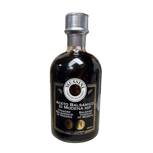 Bottle of Mussini Balsamic Vinegar on a kitchen counter with various items in the background.