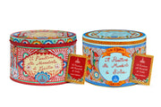 Two round tin boxes with decorative colorful designs, containing Dolce & Gabbana Sicilian Panettone alle Mandorle, with information labels in front of each tin.