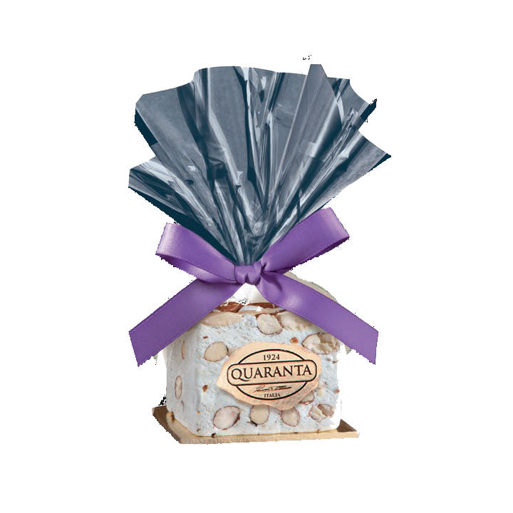 A packaged Quaranta soft nougat block with almonds, wrapped in clear plastic and tied with a purple ribbon.